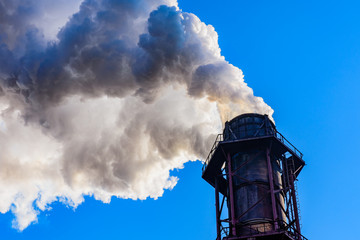 View on smoke pipe of the factory against blue sky. Environmental pollution