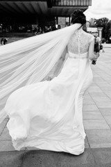Portrait of beautiful bride in wedding dress with bridal bouquet in city outdoors, back view, copy space. Wedding concept