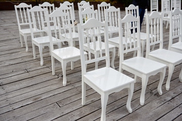 White wedding chairs with fresh flowers on each side of archway outdoods, copy space.  Empty wooden chairs prepared for wedding ceremony