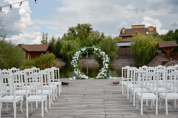 Place for wedding ceremony outdoors, copy space. Circle wedding arch decorated with flowers and chairs on each side of archway. Wedding setting