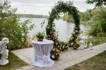 Beautiful round wedding arch decorated with flowers and greenery near lake or river outdoors, copy...
