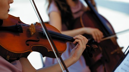Musical Orchestra Of Female Musicians Plays On The Summer Terrace Outside, Hands Holding A Violin And Bow, Close Up