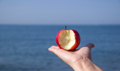 red bitten Apple in hand against the sea.  ecotourism and consumption of natural and organic fruits. Concept harmony between recreation and ecology. diet based primarily on plant-based foods.