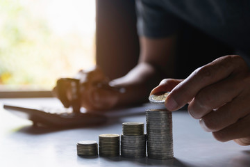 Men are using calculator about save money and put coin on stack also coins on desk in the office.