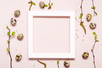 White Frame with quail eggs and blooming twigs over pink pastel background. Happy easter natural concept