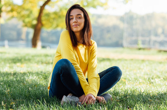 Horizontal image of a pretty happy young teenage girl relaxing outside in nature green park. A pleasant happy young beautiful student female sitting outdoors in city park.