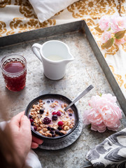 Hand mit Müsli, Milch und frsichen Beeren auf einem rustikalen Tablett im Bett, romantisches Frühstück