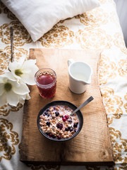 Romantisches Frühstück mit Müsli, Milch und frischen Beeren auf einem Serviertablett im Bett,...