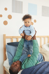 Fototapeta premium Portrait of happy African-American father playing with little son while lying on bed at home