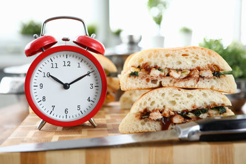 Red alarm clock with sandwich stands on wooden table closeup background. Fast food delivery concept.