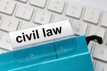 civil law is on a label of a blue hanging file. In the background a computer keyboard