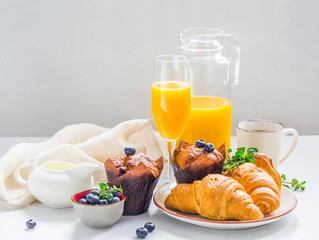 Continental breakfast: blueberries muffins, orange juice, croissant, coffee, milk.