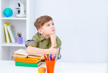 Single dreaming boy at the desk at the home enjoy books. Front image with boy keeping left hand on the book . European boy explore books. Pupil loves education, preparing for school.