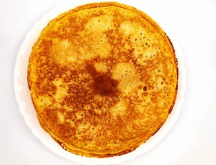 Fresh pancakes fried in sunflower oil lie in a white round plate. Pancakes are thin, made of flour, eggs, sugar, and soda