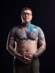 Hipster, bare-chested millennial young male body covered in tattoos. Make a tattoo with skulls artist. To hammer a breast. Rocker informal with an earring in his ear tattooed