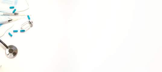 Long wide medical banner with stethoscope, sterile surgical masks, vial with vaccine, big blue pills and syringes on white background. Vaccination and health care concept. Epidemic prevention concept.