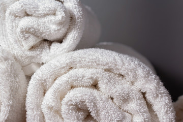 Close up photo of white terry towels. Personal towels for hotel guests. Dark bathroom. Storage in rolls.