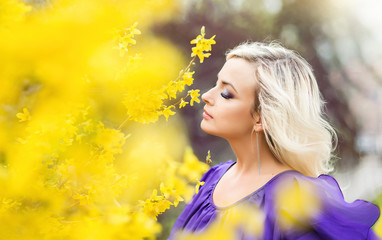 portrait of a girl on a background of yellow flowers. Spring photo with a beautiful woman in a purple dress with blooming forsythia. The concept of perfumery and cosmetics