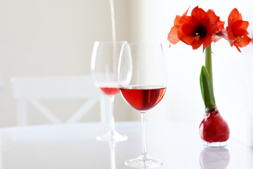 Two glasses with red wine and a red amaralis flower on a white table in a white interior. Contrast photo in a stylish white room. Minimalism