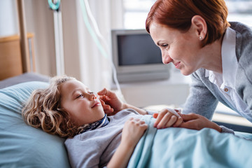 Caring mother visiting small girl daughter in bed in hospital.