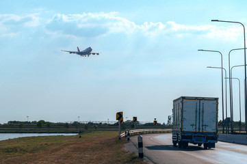 Fototapeta premium Flying Passenger Jet Plane on The Sky over The Container Truck Running on The Road