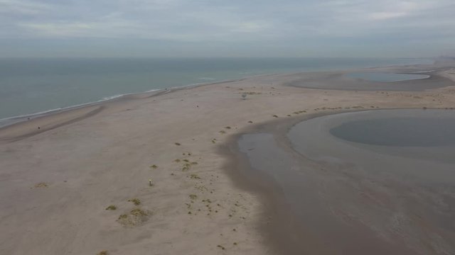 Aerial view that slowly winds around a large beach with a few people walking in the distance 
