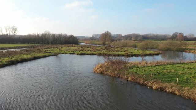 A large river that is meandering through bright green colored grass of the surrouding meadows in europe