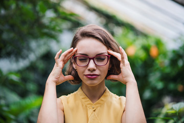 Tired young woman standing in greenhouse in botanical garden.