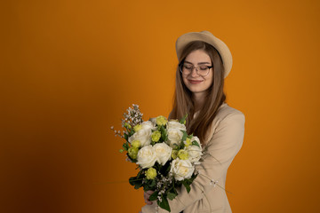 Joyful girl in glasses holding flowers on yellow background