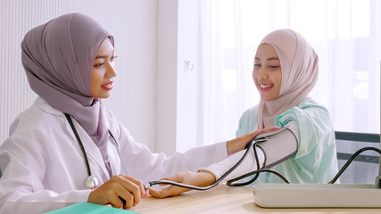 Muslim female doctor checking up patient's blood pressure at hospital room.