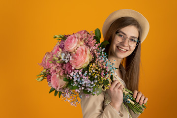 Cheerful young woman with flowers smiling isolated on yellow background