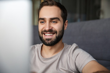 Man indoors at home on sofa using laptop computer.