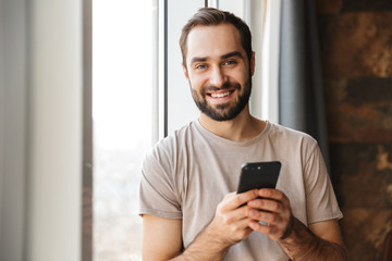 Cheery young man indoors chatting by mobile phone.