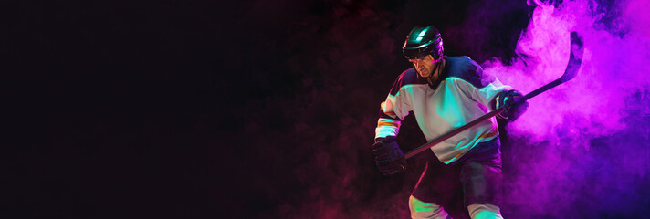 Male hockey player with the stick on ice court and dark neon colored background. Sportsman...