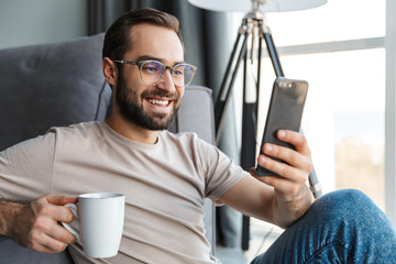 Optimistic young man indoors drinking coffee