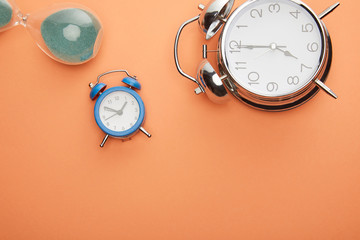 top view of alarm clocks and hourglass on peach background