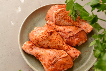 Raw chicken in a plate. Marinated meat, with oregano, herbs and paprika. Raw chicken legs, step by step cooking. Close-up, gray light background.