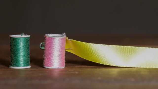 Colorful plastic spools of sewing threads with sewing needle and red thimble with yellow ribbon timelapse