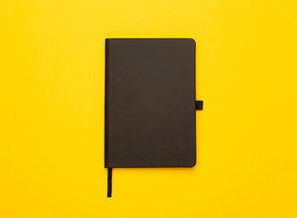 Black notebook isolated on yellow background. Flat lay or Top view angle.