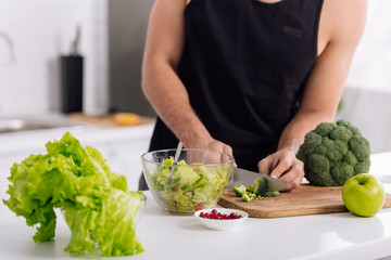 cropped view of man cutting broccoli on chopping board