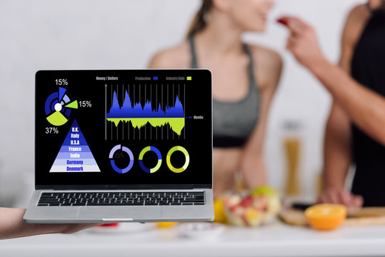selective focus of laptop with charts and graphs with numbers near couple in kitchen