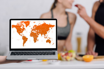 selective focus of laptop with world map on screen near couple in kitchen