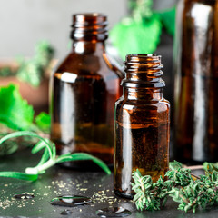 Essential oils in a brown glass bottle, thyme, rosemary and mint on the table, dark background. Herbal essential oil, aromatherapy.