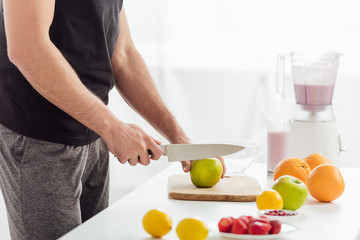 Obraz na płótnie Canvas cropped view of man cutting apple near fresh fruits and smoothie