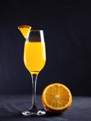 A glass of Mimosa cocktail with sparkling champagne and orange juice on a black concrete table