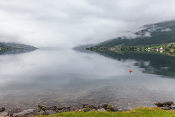 Norwegian fjord and mountains surrounded by clouds, ideal fjord reflection in clear water. selective focus.