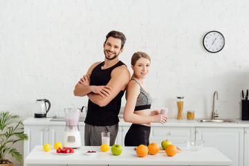 sportive man with crossed arms near happy woman with smoothie in glass