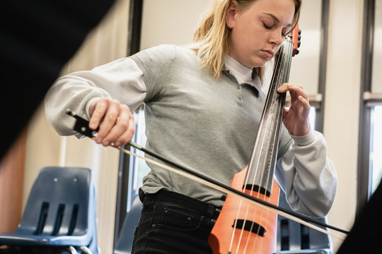 Female high school musician playing an electric cello during classroom rehearsal