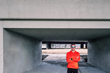 Attractive sportsman standing in urban concrete area with hands crossed and looking at camera.