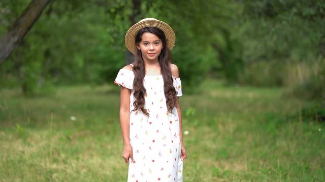 Trandy Teenager Girl Posing For Social Network Pictures On Camera In Garden. Young Girl Wearing Sun Hat Stay In Park And Looks To Camera.